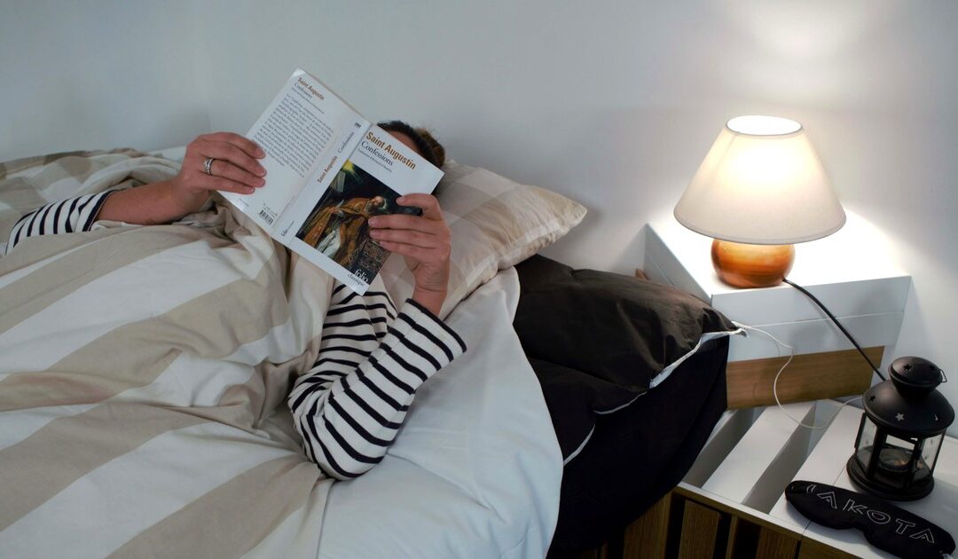Une personne lit au lit, lampe de chevet allumee, sur un surmatelas IAKOTA relie a la terre