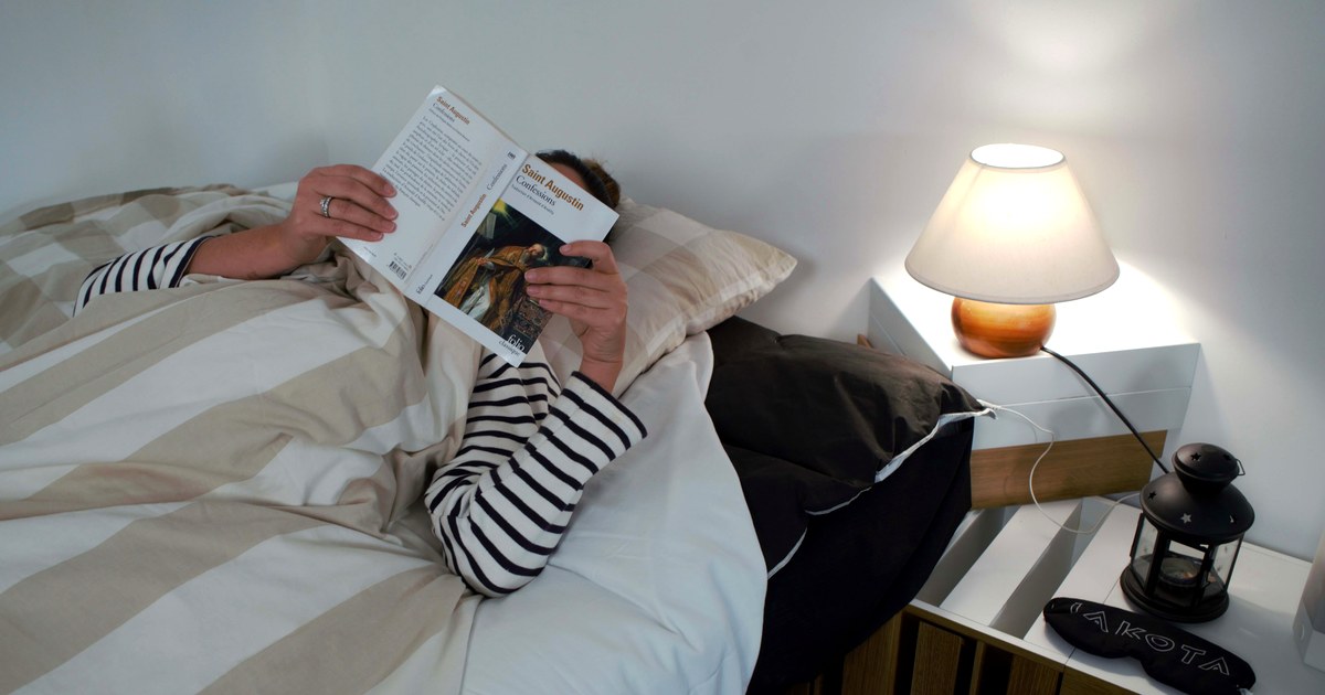 Une personne lit au lit, lampe de chevet allumee, sur un surmatelas IAKOTA relie a la terre